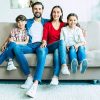 Family relax on the couch. Happy beautiful young parents are smiling, hugging and playing with them kids at home together